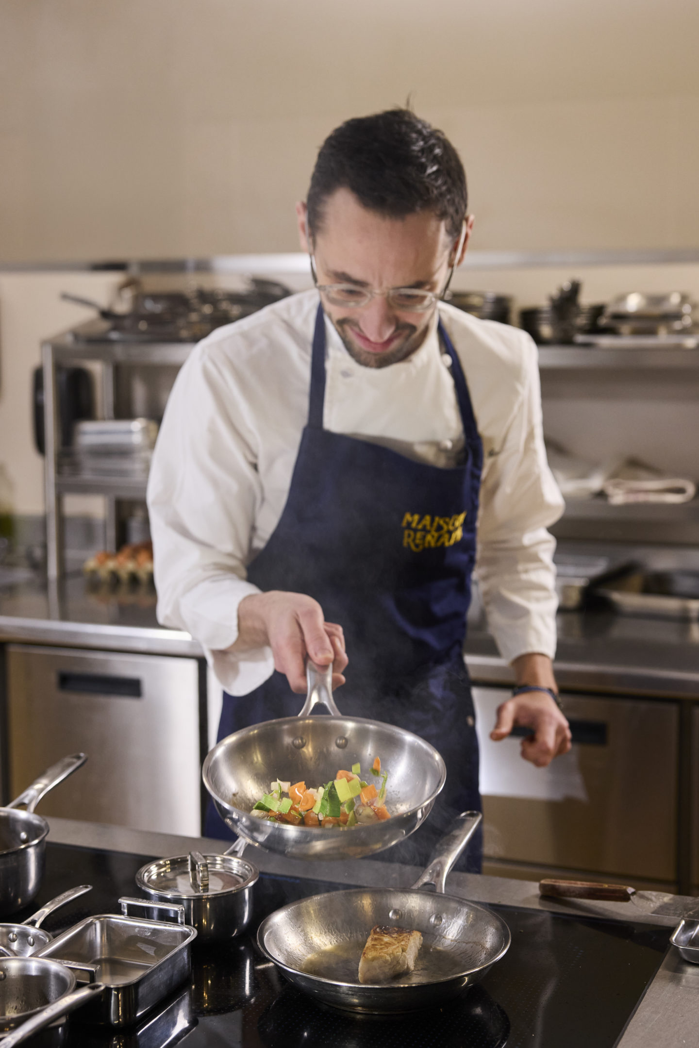 Un chef en train de cuisiner dans sa cuisine professionnelle avec une poële en inox cristel