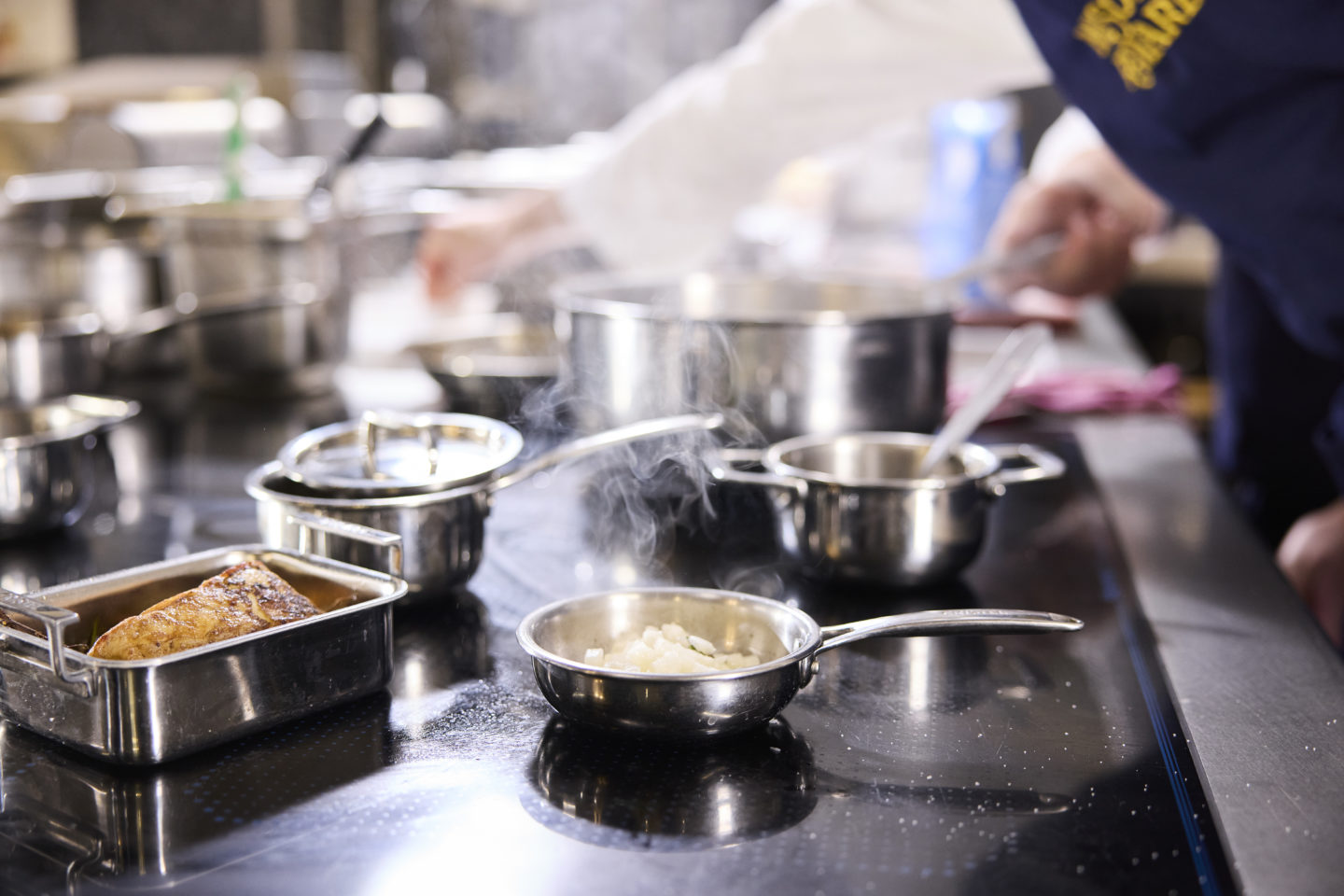 Ustensiles en inox sur plaques de cuisson dans une cuisine professionnelle avec les bras d'un chef en action
