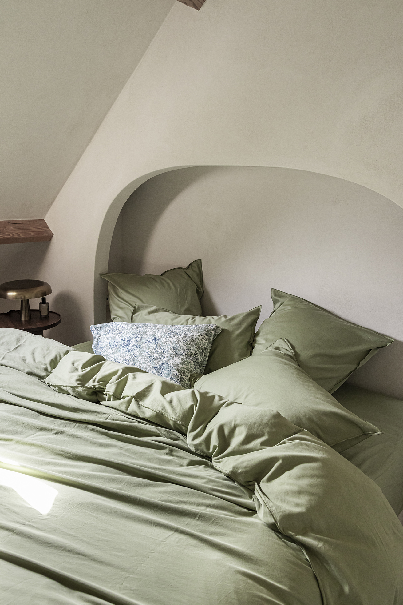 Un lit avec une parure en satin couleur sauge dans une chambre de couleur beige
