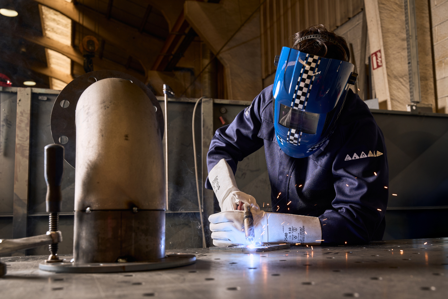 Un homme en tenue Invict Light Molinel bleue fait de la soudure dans une chaudronnerie