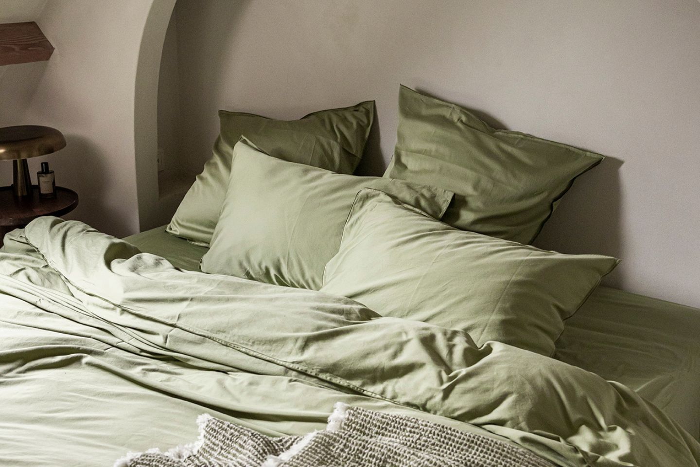 Un lit avec une parure couleur sauge dans une chambre de couleur beige