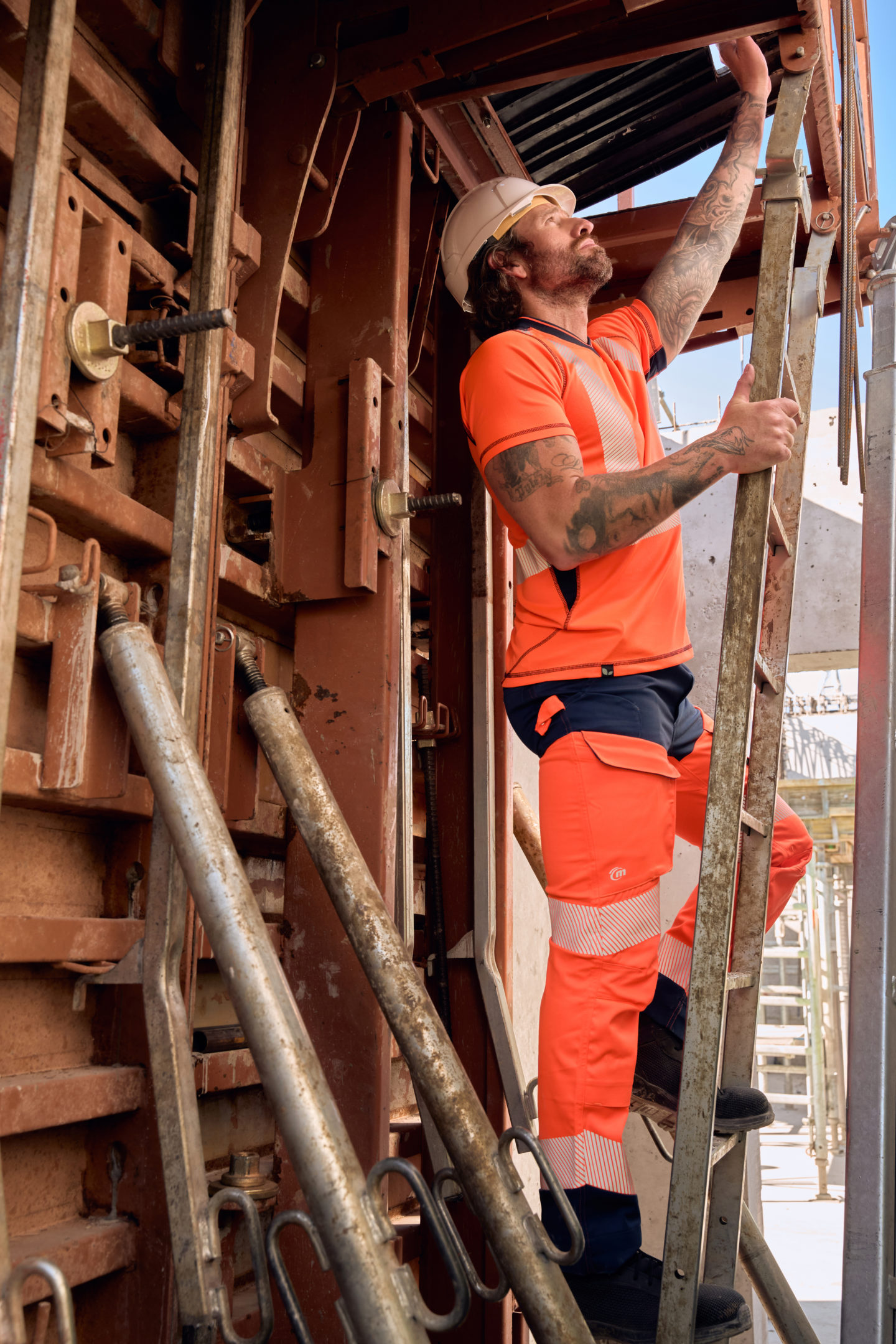 Homme en tenue fluorescente orange Molinel en train de monter à une échelle sur un chantier