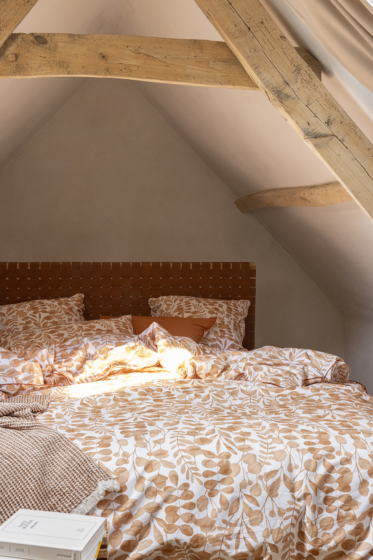 Un lit avec une parure en chanvre couleur naturel et terracotta dans une chambre de couleur beige