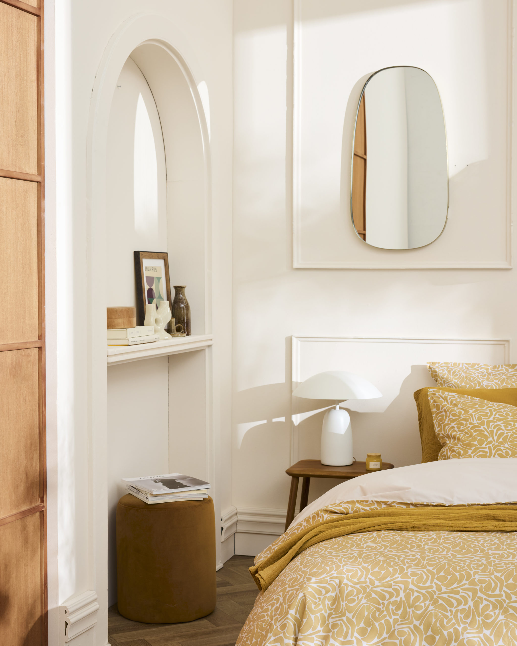 Un lit avec la parure Hera aux motifs jaunes dans une chambre épurée avec des moulures, une porte en bois et des éléments de décoration