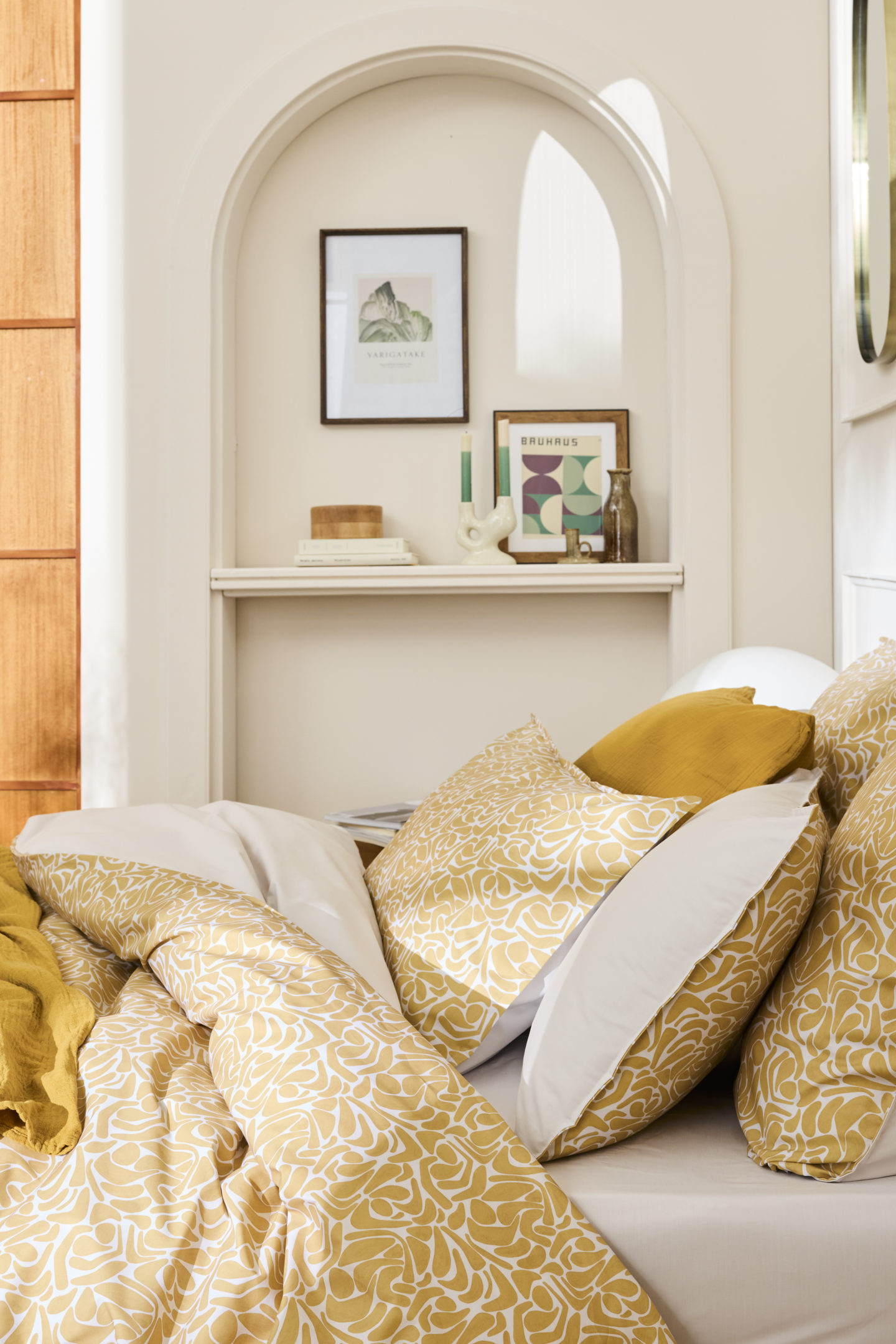 Focus sur le haut du lit avec la parure Hera aux motifs jaunes dans une chambre épurée avec des moulures, une porte en bois et des éléments de décoration