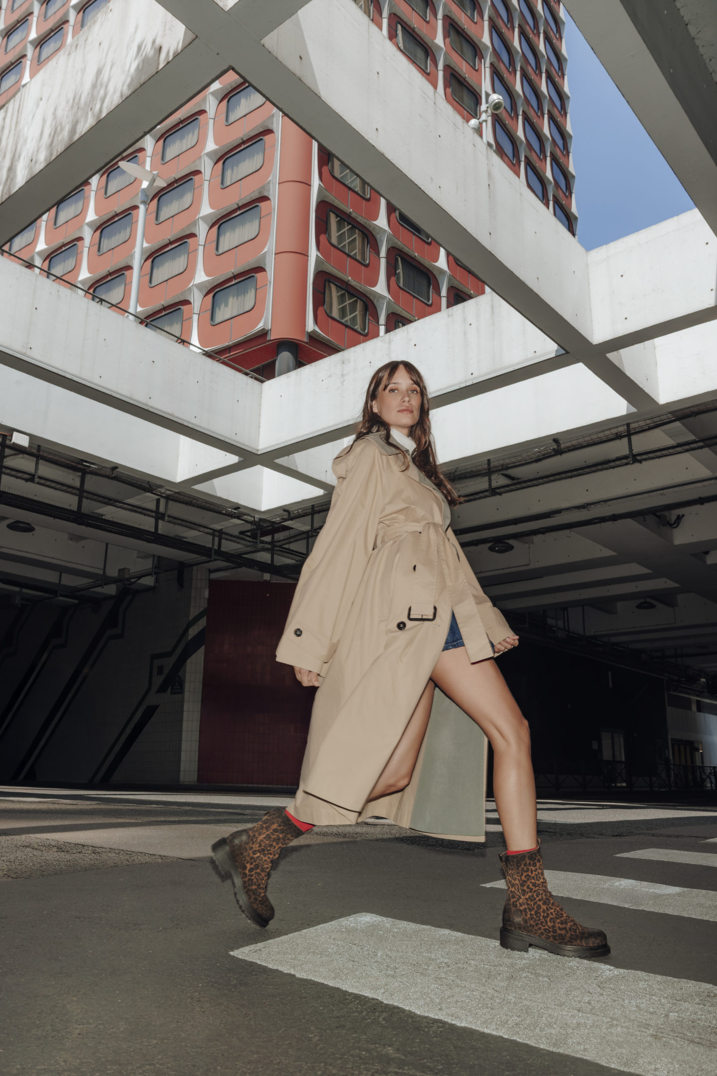 Femme qui marche dans un quartier mélangeant architecture brute, béton et ciel ouvert