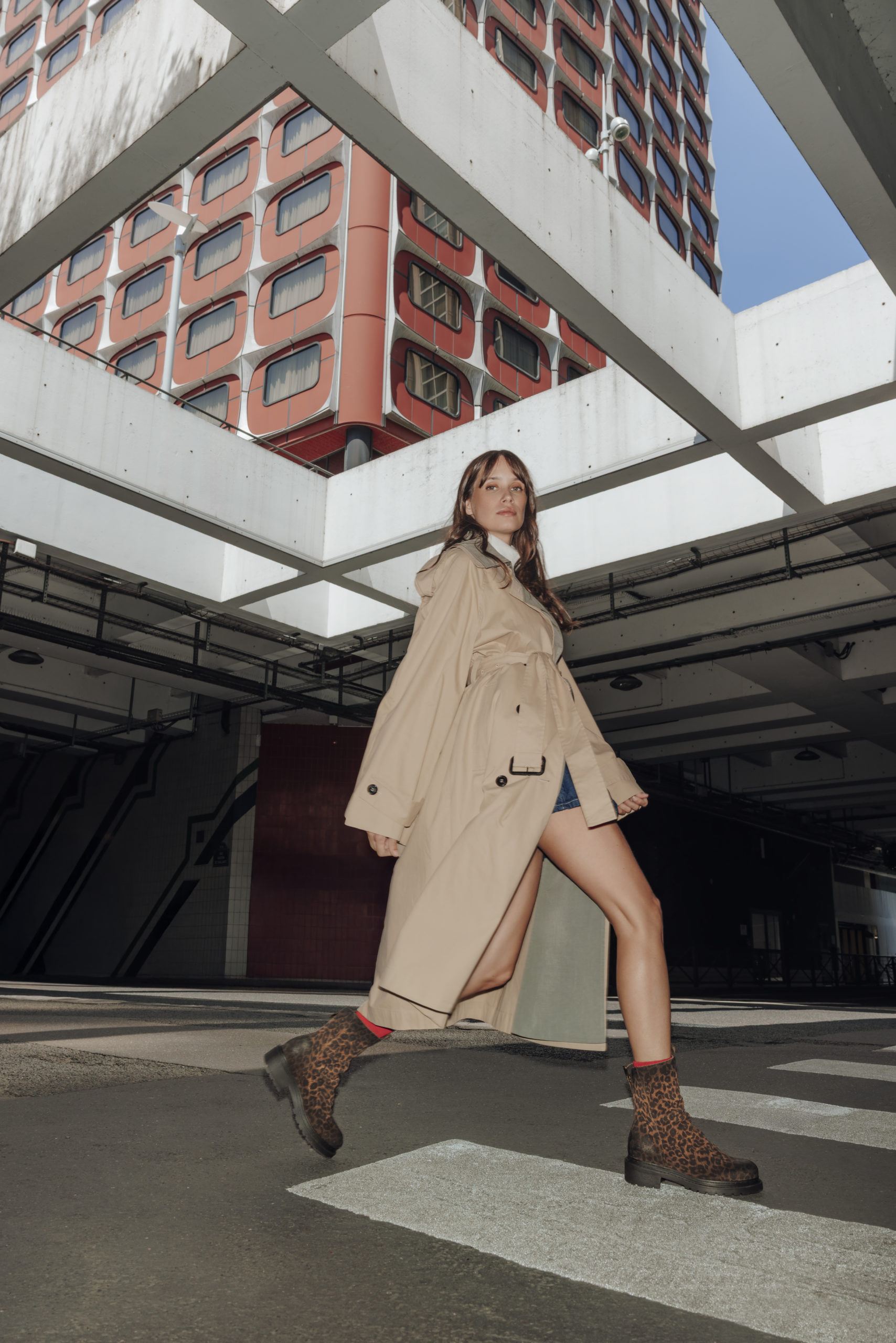 Femme qui marche dans un quartier mélangeant architecture brute, béton et ciel ouvert