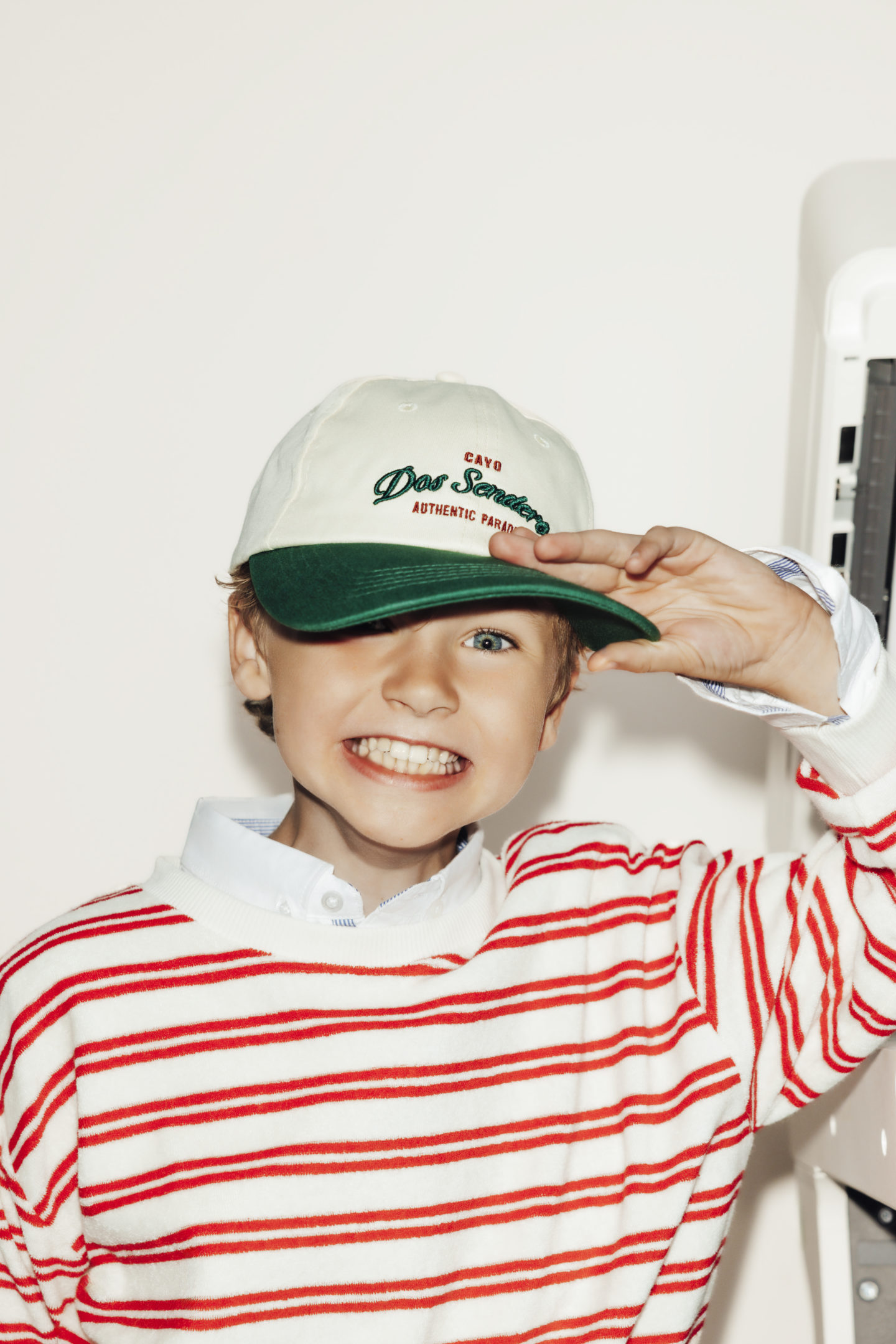 Petit garçon qui sourit en tenant sa casquette blanche et verte sur un fond blanc