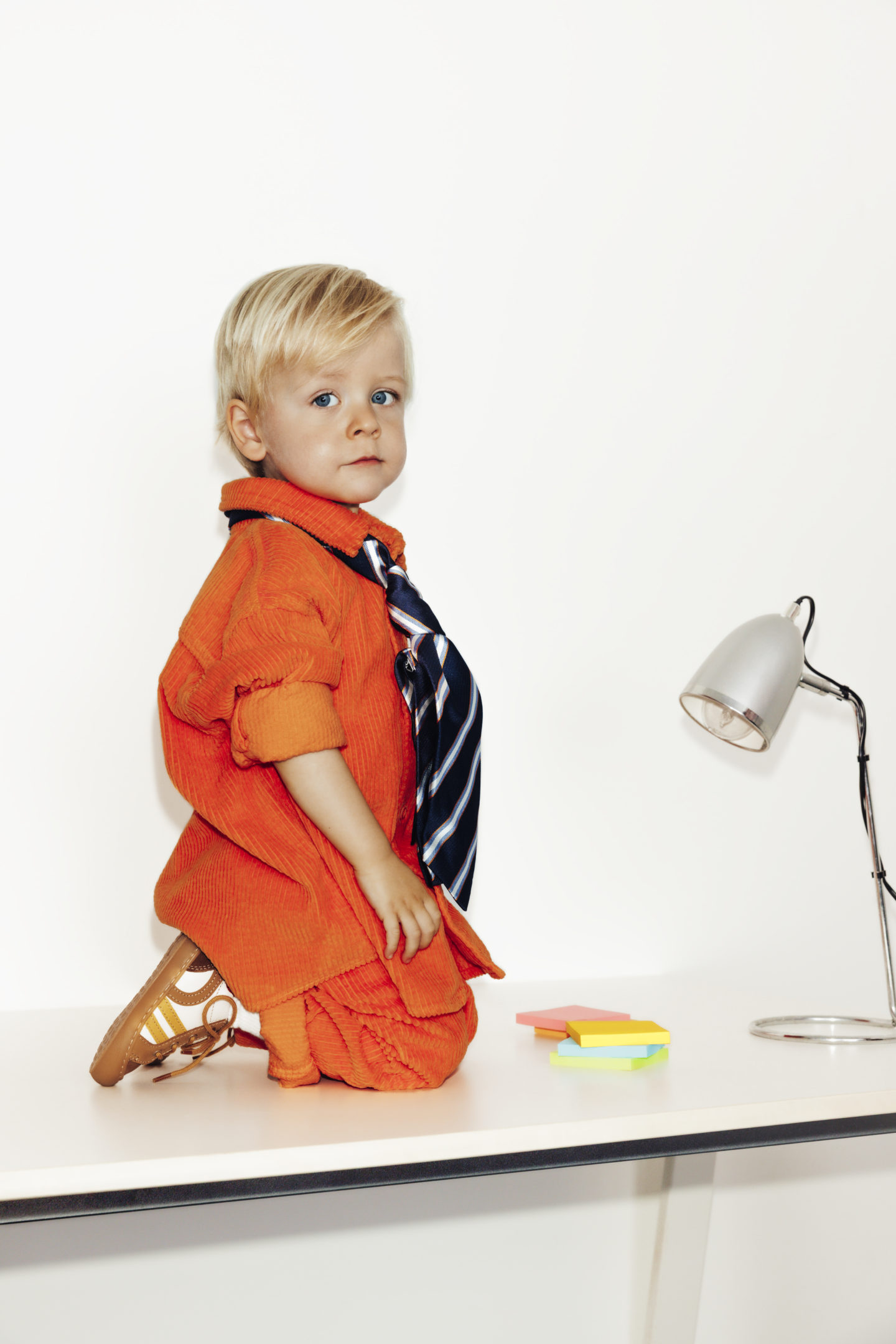 Enfant habillé en orange avec des sneakers Jef à genoux sur un bureau avec des posts-it et une lampe
