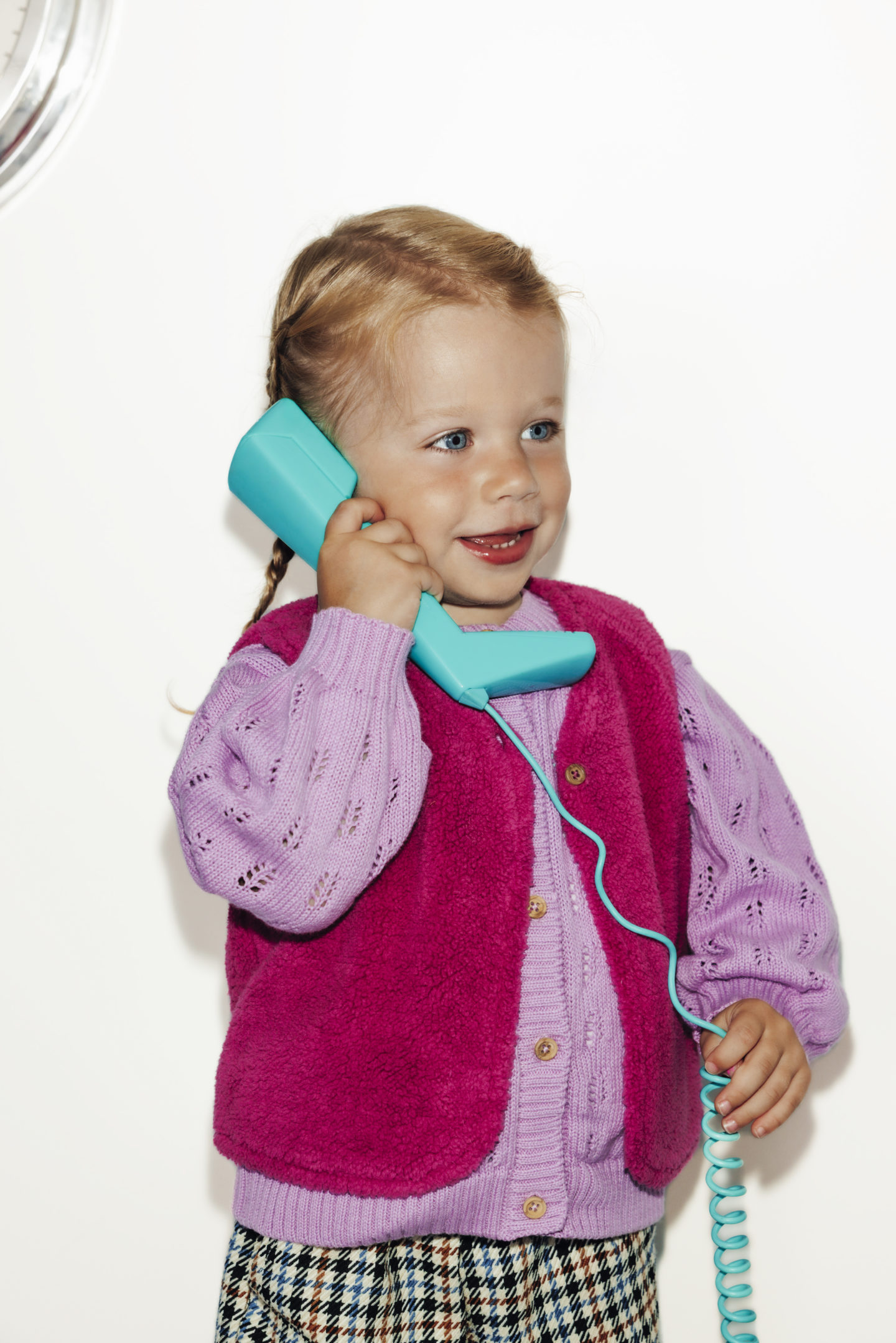 Petite fille habillée en rose avec un téléphone vintage bleu sur fond blanc