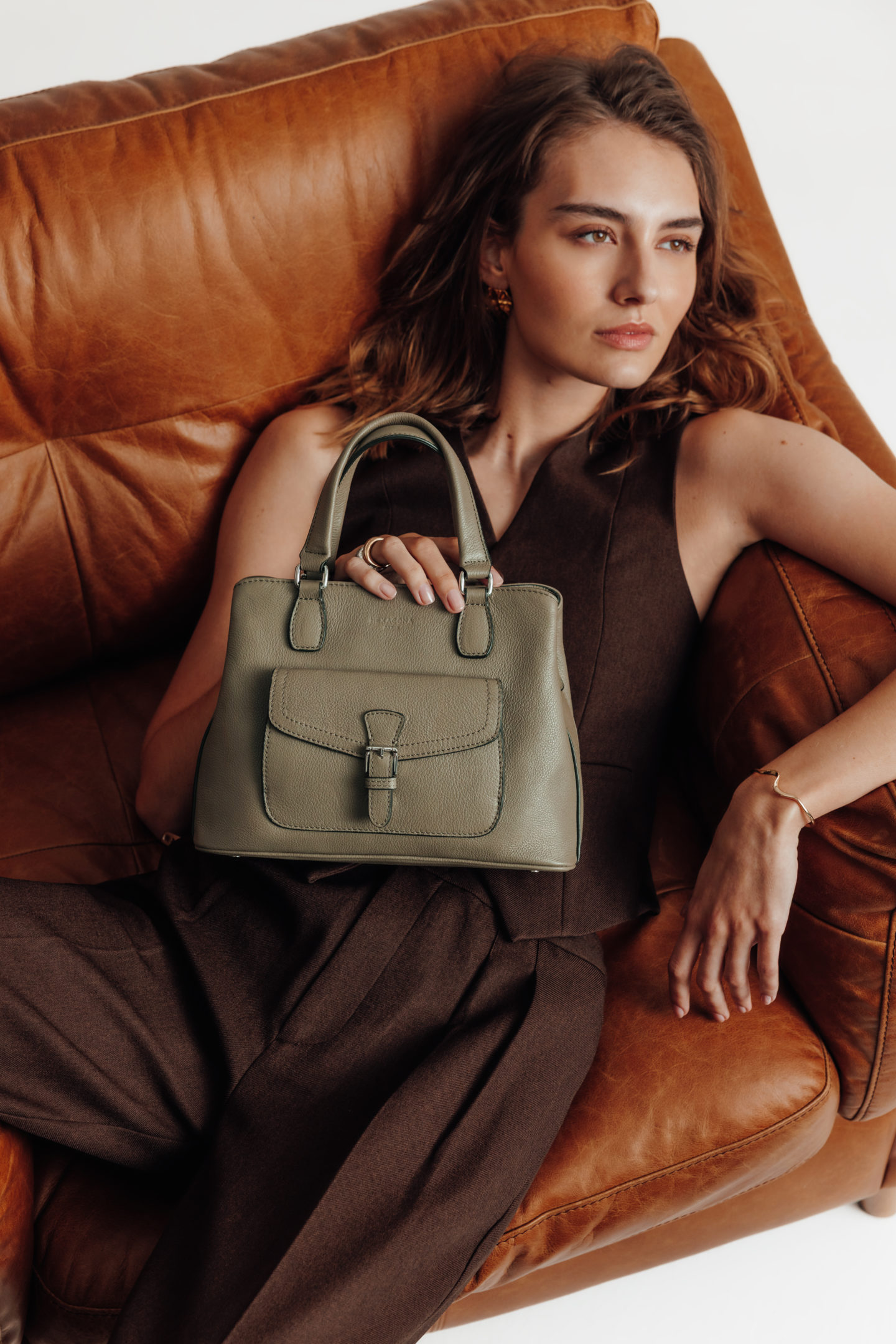 Zoom d'une jeune femme assise/allongée dans un fauteuil cognac tenant un sac à main