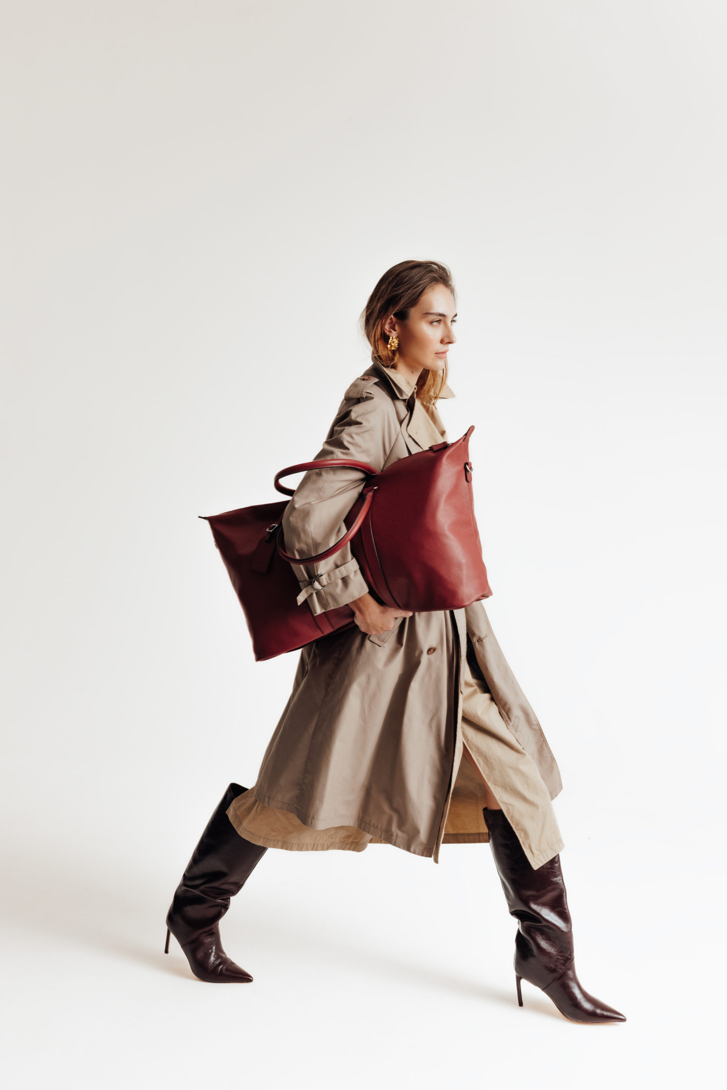 Jeune femme marchant qui porte un sac de voyage à hauteur de coude avec un fond de studio blanc